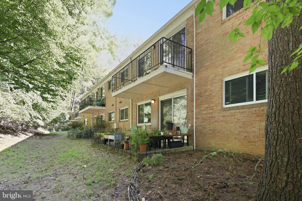 Brick residential building with ground-level patios and balconies beneath mature trees.