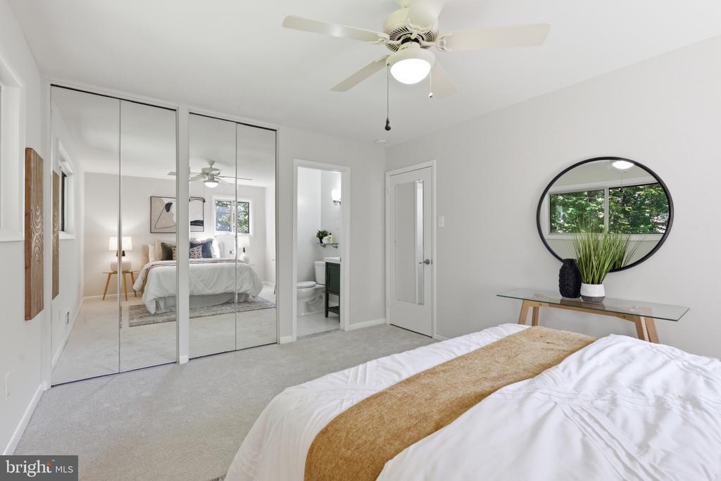 Bedroom with mirrored closet doors, a ceiling fan, and an adjoining bathroom.