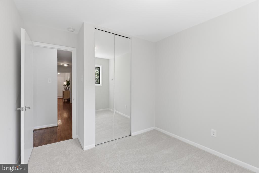 Empty bedroom with mirrored closet doors and an open doorway to a wood-floored hall.