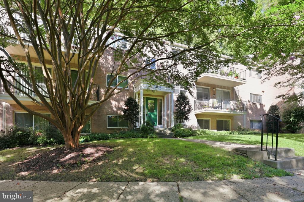 Apartment building entrance with a green door, balconies, and mature trees.