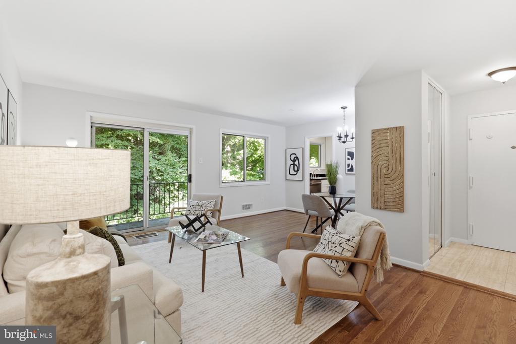 Furnished living room with a glass coffee table, hardwood floors, and sliding doors overlooking trees.