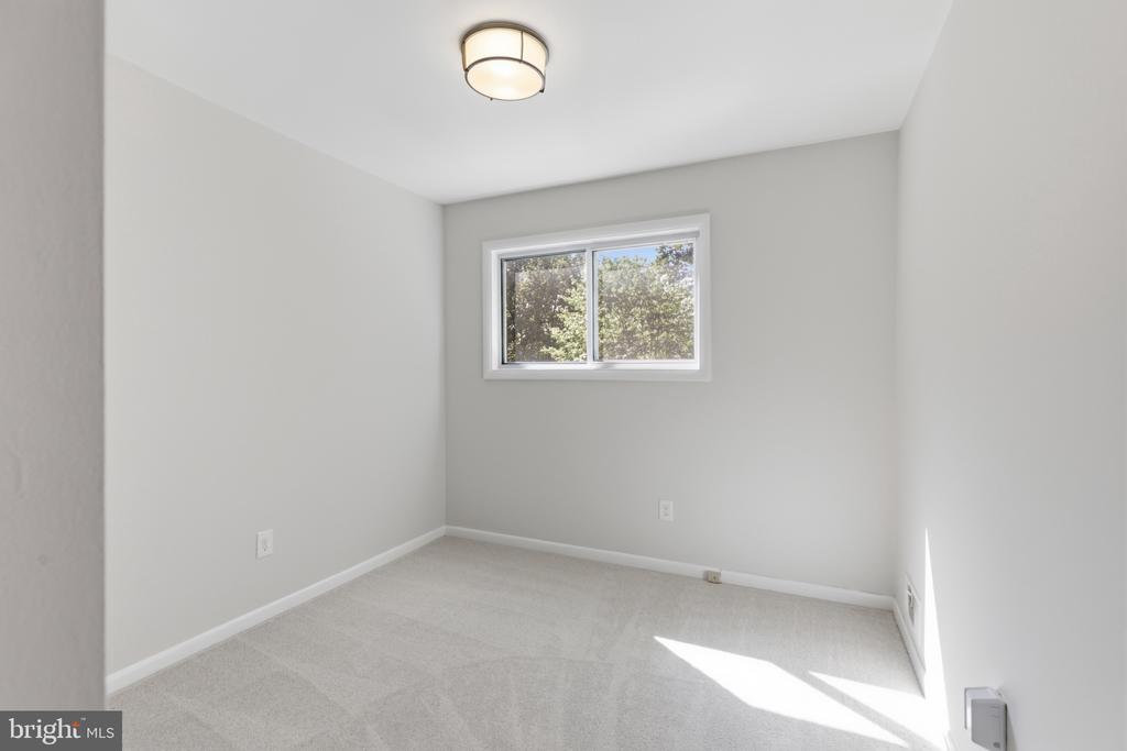 Empty bedroom with pale carpet, a ceiling light, and a small window overlooking trees.