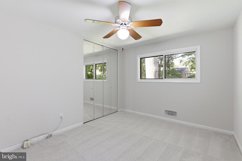 Empty bedroom with mirrored closet doors, a ceiling fan, and a window overlooking trees.