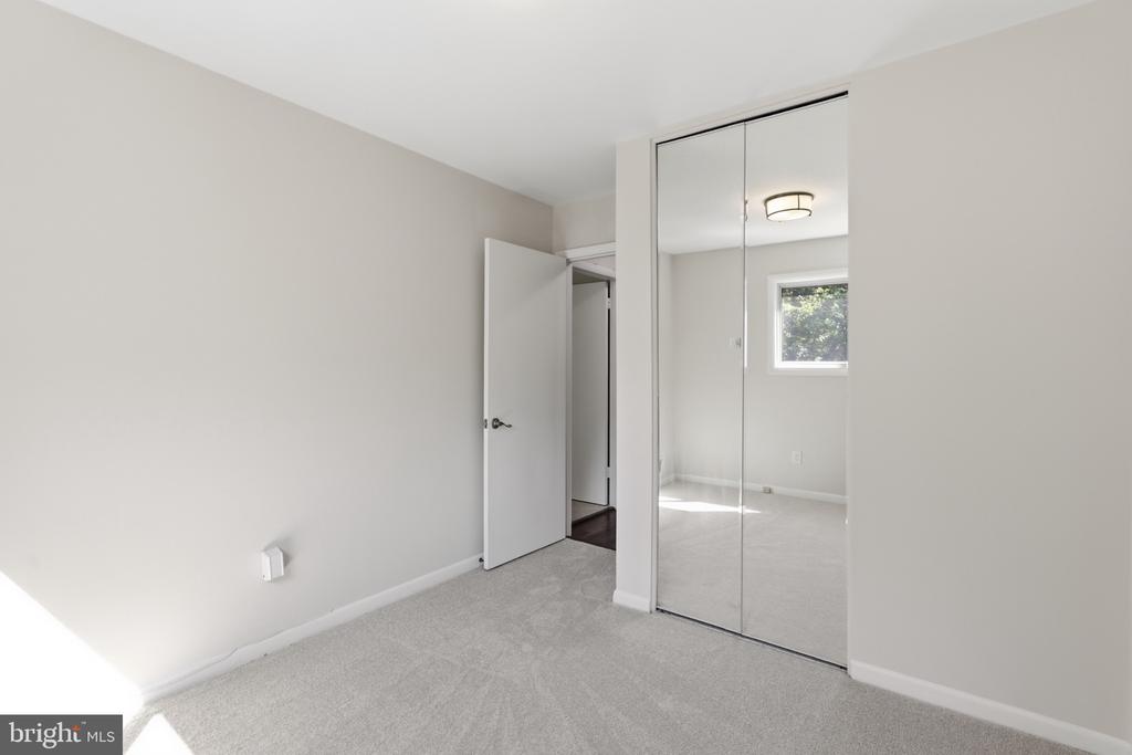 Empty carpeted bedroom with mirrored closet doors and an open doorway.