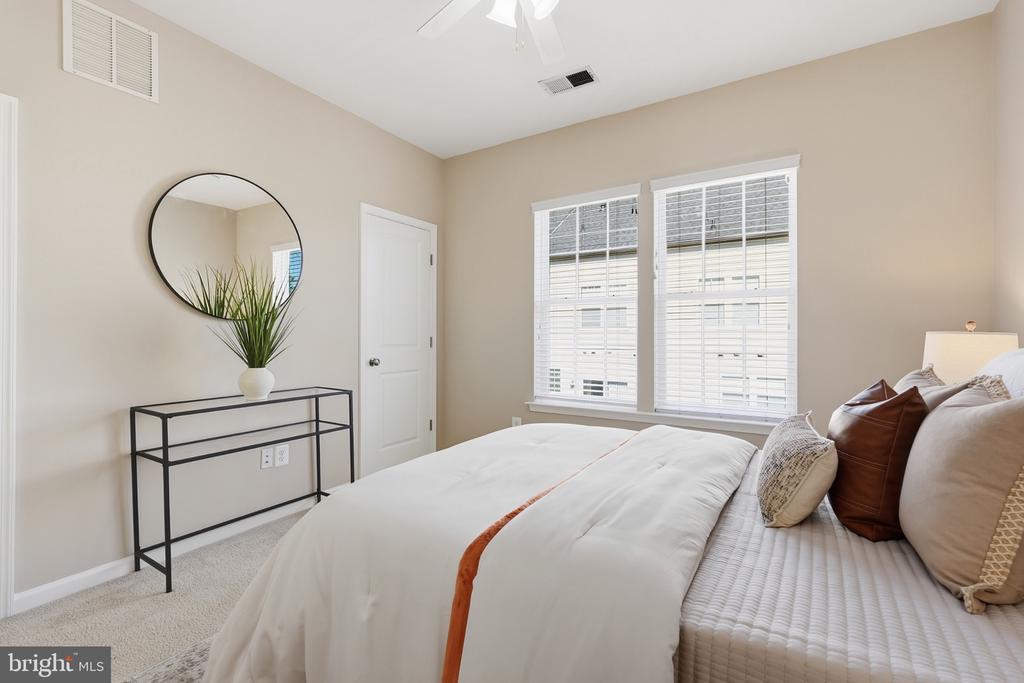 Furnished bedroom with a white bed, two bright windows, and a round mirror above a console table.