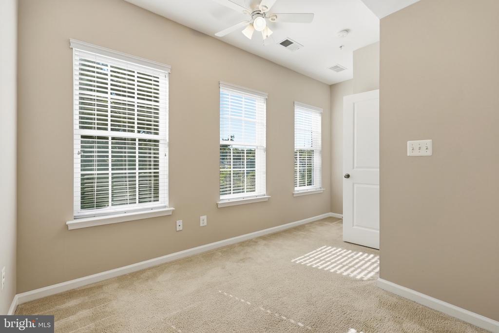 Empty bedroom with three blind-covered windows, beige carpet, and a ceiling fan.
