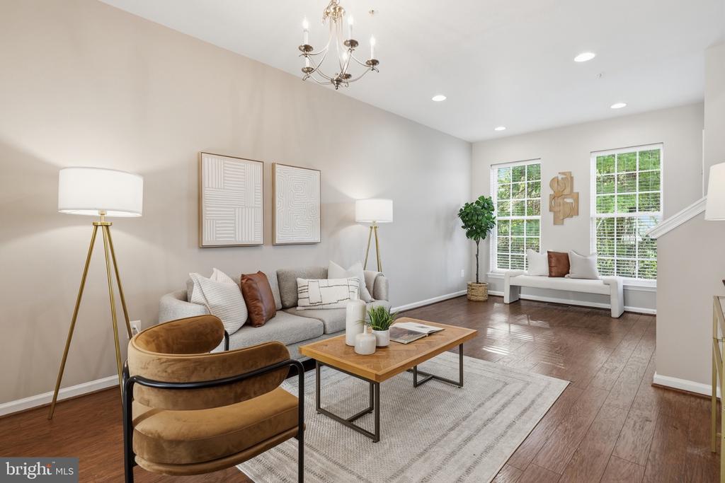Staged living room with a gray sofa, brown chairs, tall windows, and dark hardwood floors.