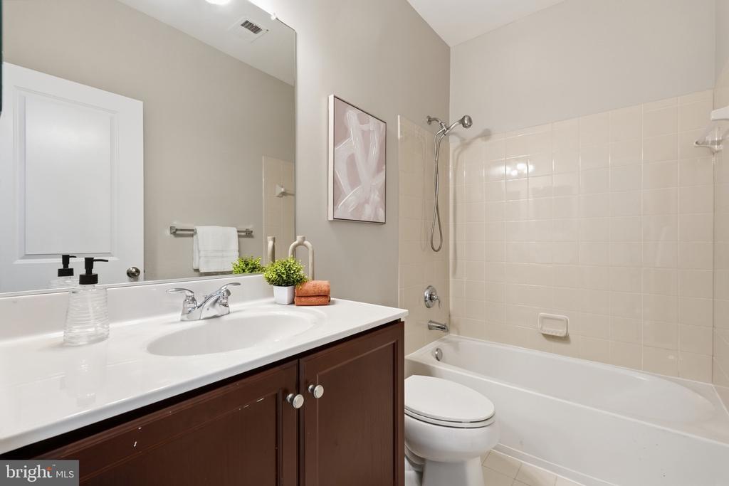Bathroom with dark wood vanity, large mirror, and white tiled tub-shower combination.