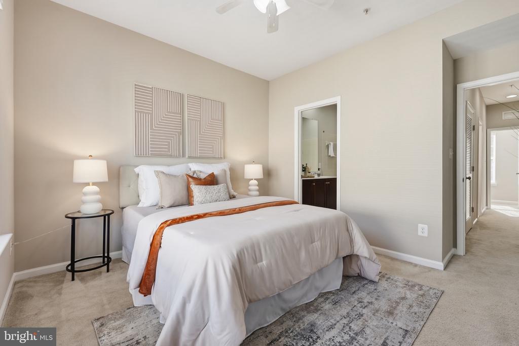 Furnished bedroom with a white bed, rust-colored accents, geometric wall art, and an en-suite bathroom doorway.