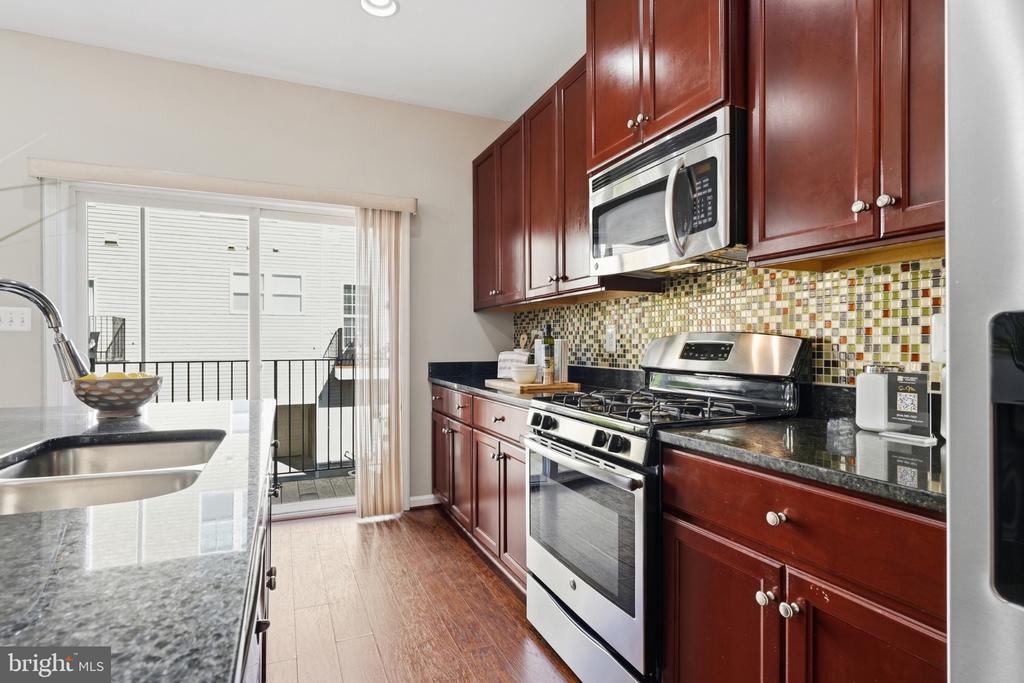 Kitchen with cherry cabinets, granite counters, mosaic tile backsplash, and stainless steel appliances.