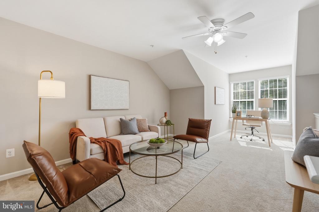 Living room with cream sofa, brown leather chairs, glass coffee table, and adjoining desk by bright windows.