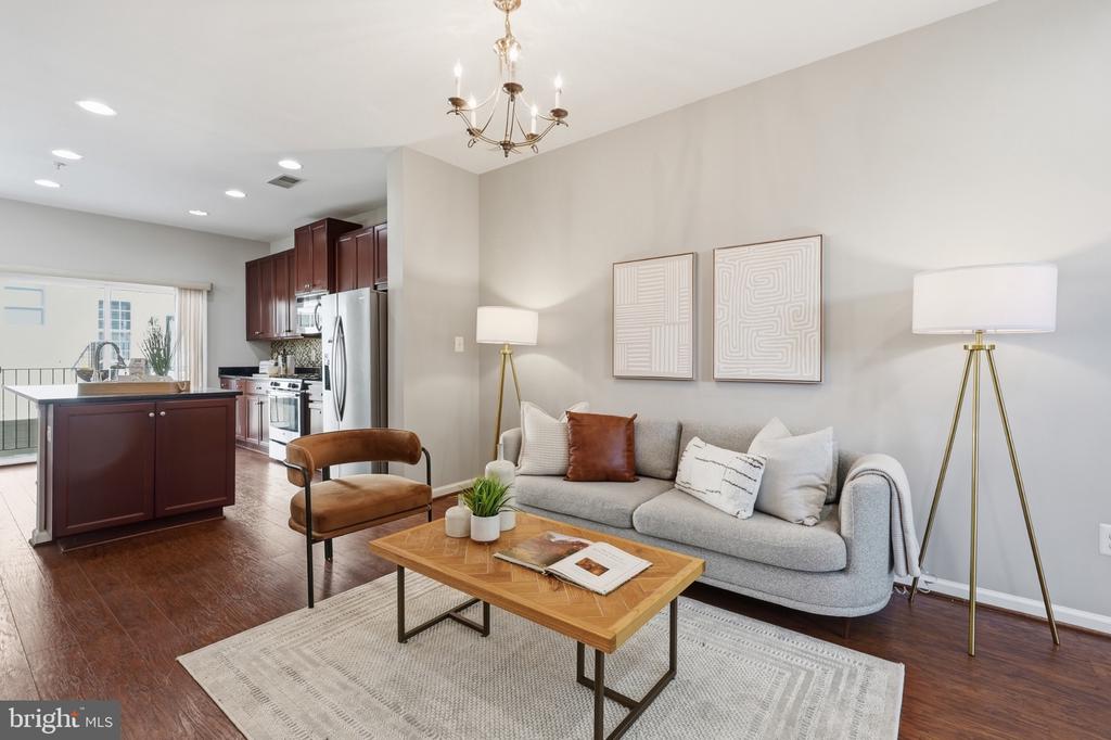 Staged living room with gray sofa and wood coffee table opening to a kitchen with burgundy cabinets.