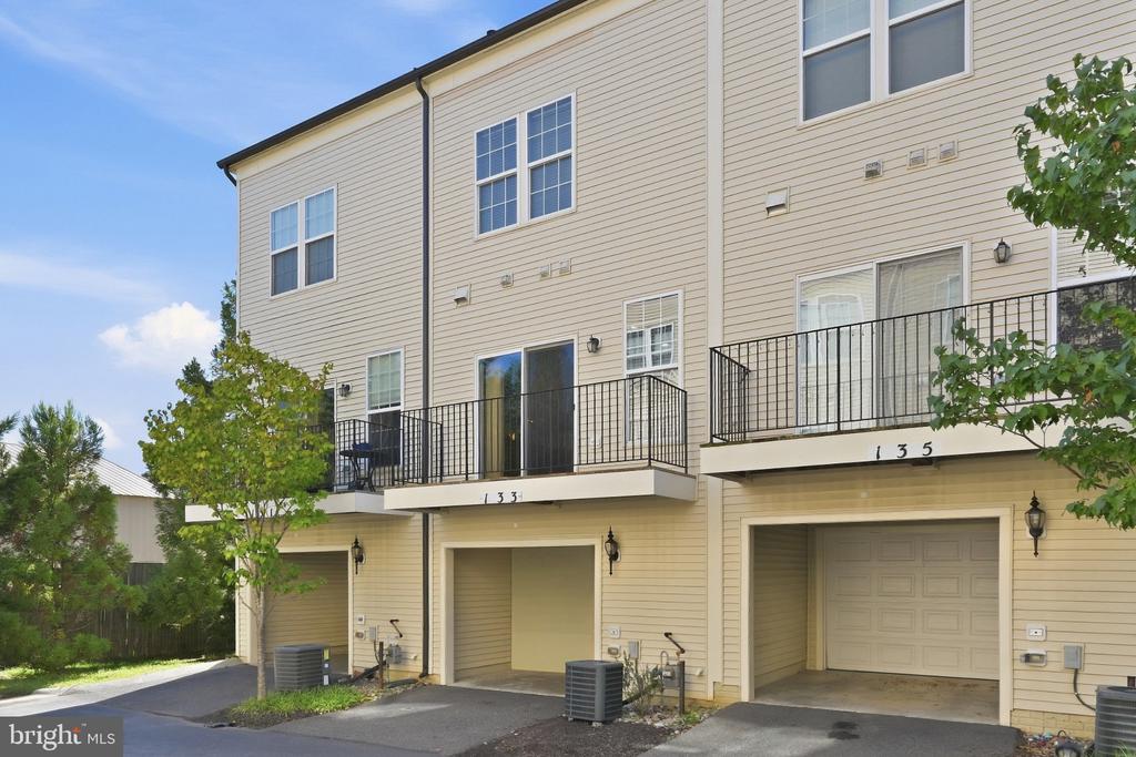 Beige townhome rear with raised decks and garage doors beneath units 133 and 135.