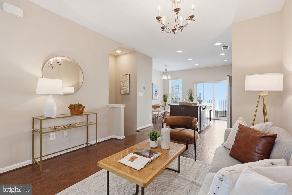 Staged living room with hardwood floors, a wood coffee table, and an open kitchen leading to a balcony.