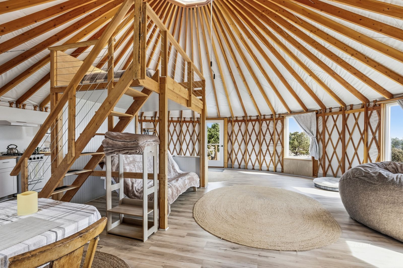 Furnished circular timber interior with a loft staircase, beds, and a vaulted exposed-beam ceiling.
