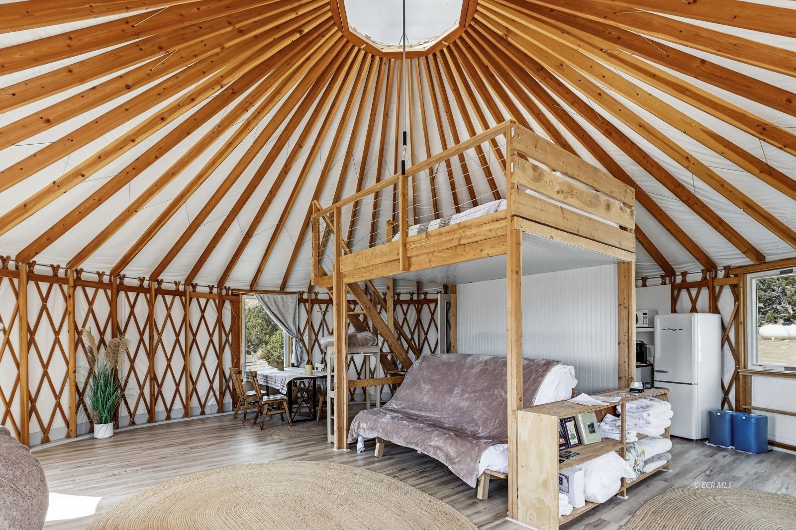 Yurt-style bedroom with a loft bed, exposed timber rafters, and a small dining area.