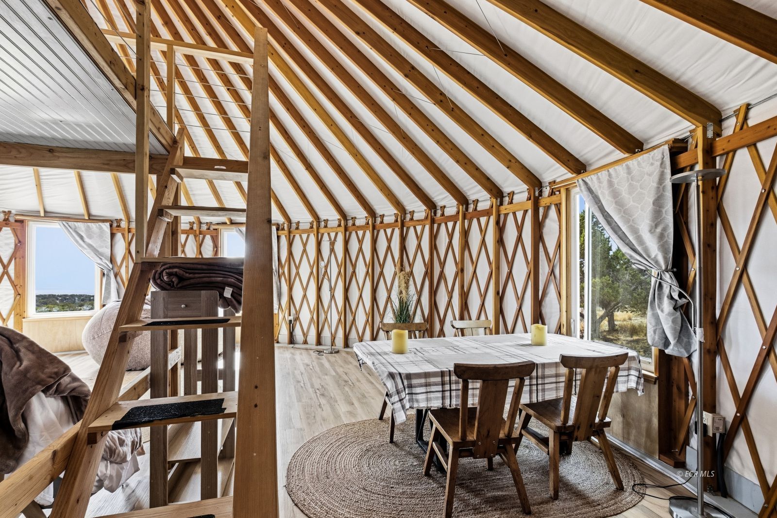 Dining area in a yurt with exposed timber framing, a round rug, and large windows.