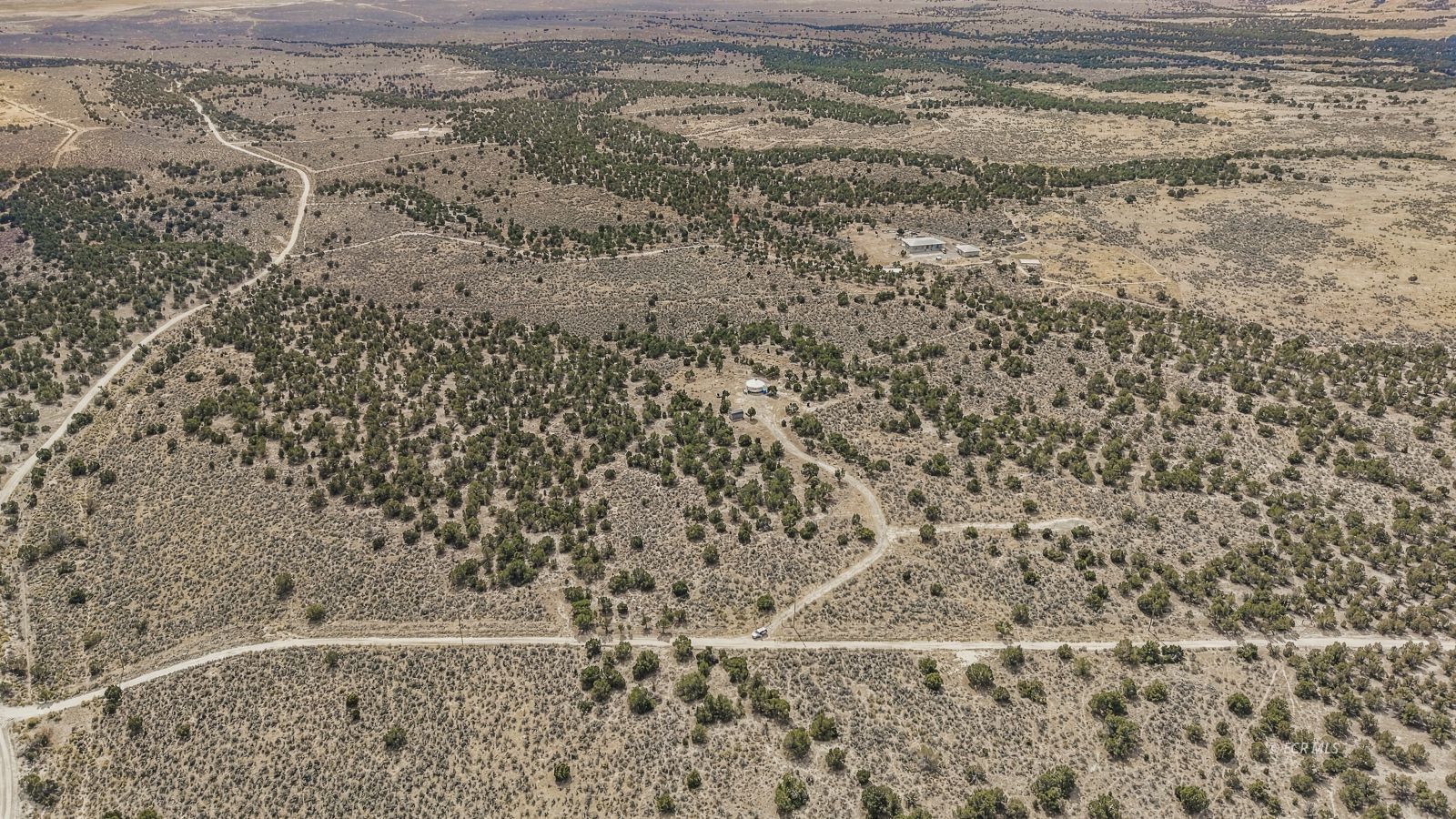 Aerial view of a rural property with sagebrush, scattered trees, dirt roads, and several buildings.