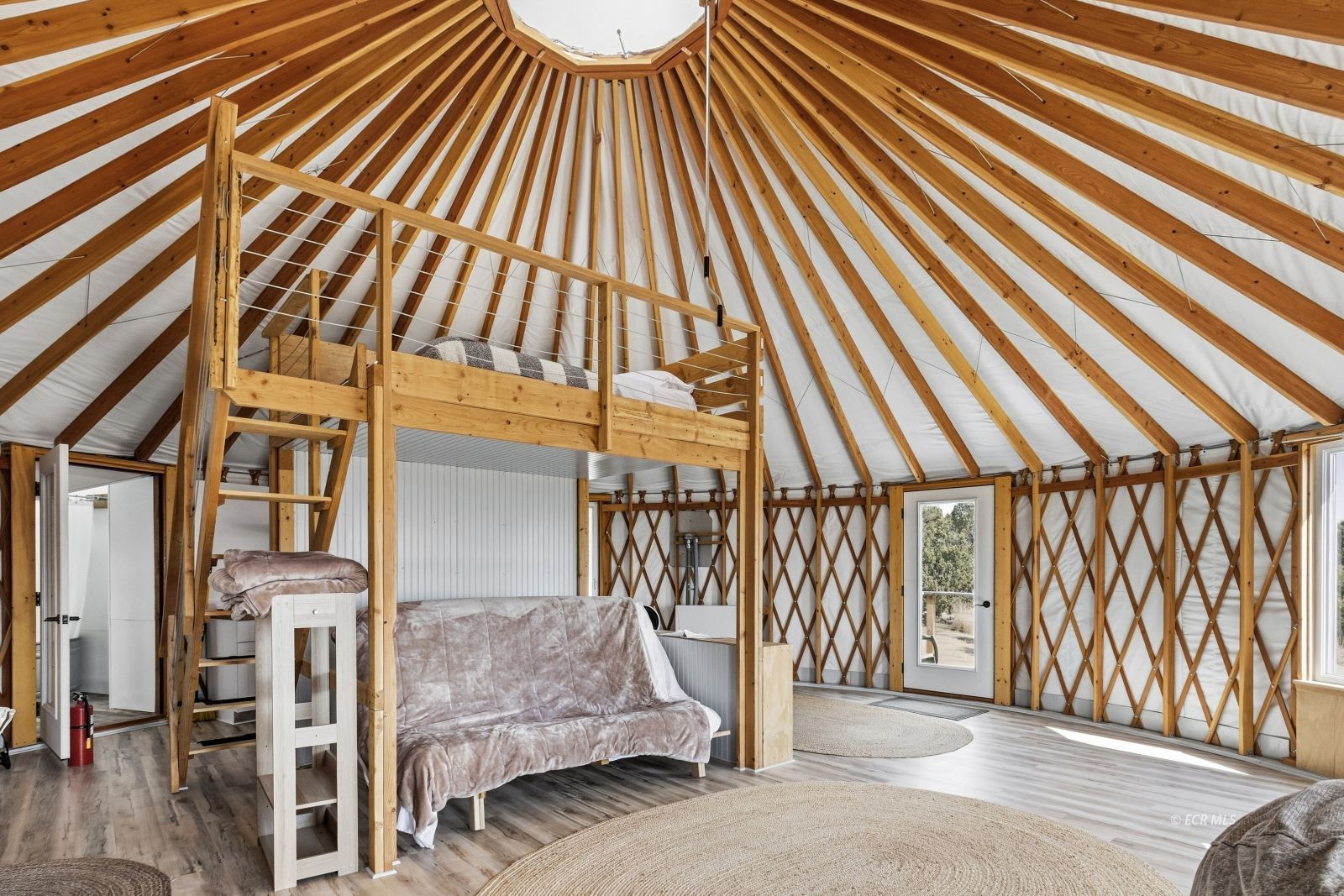 Furnished circular timber interior with a loft bed, sofa, and dramatic exposed rafters.