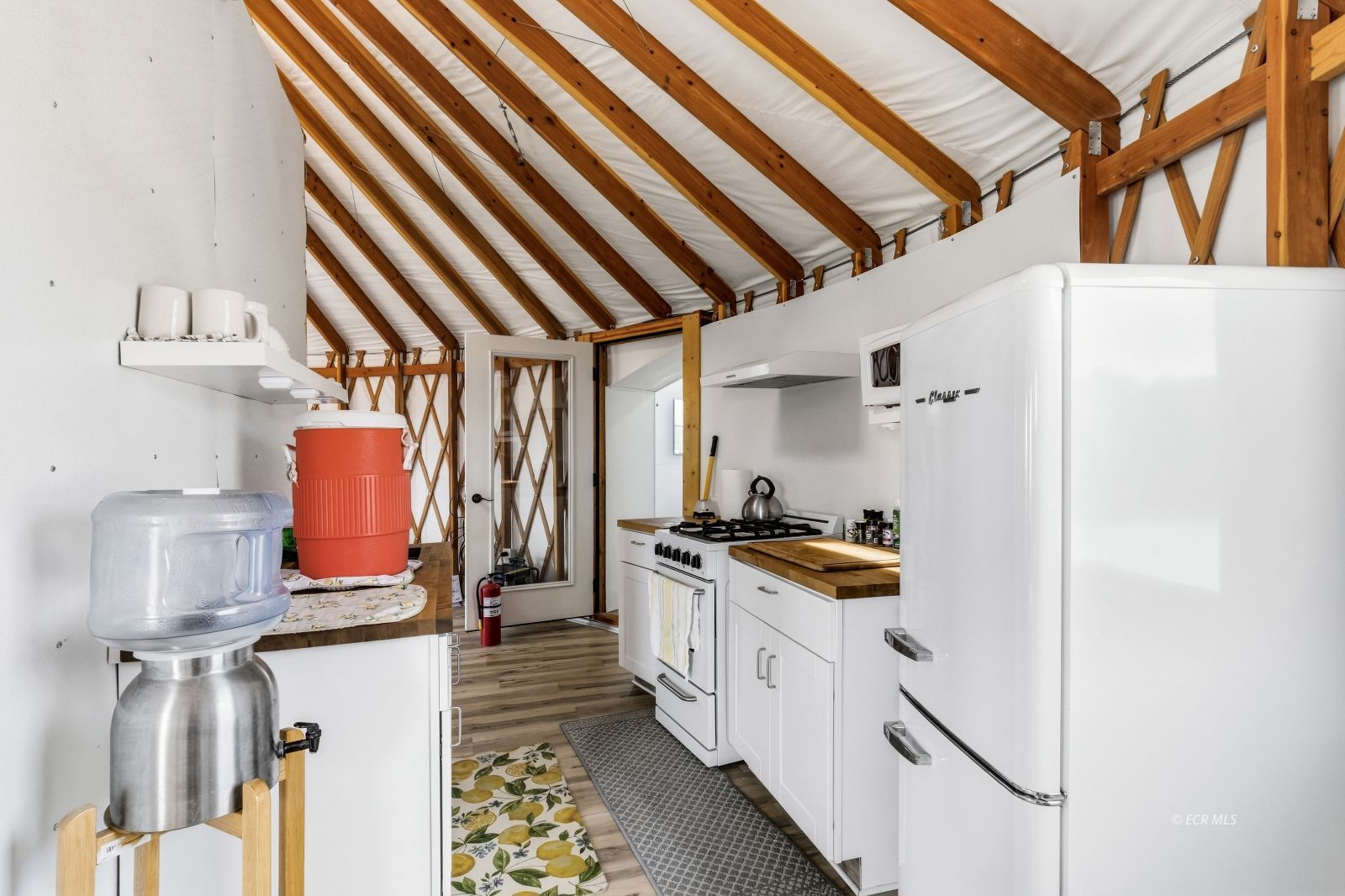 Compact kitchen with white appliances beneath exposed timber rafters.