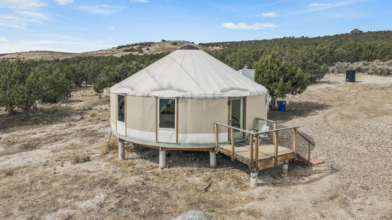 Round canvas yurt with a small raised deck on a scrub-covered rural lot.