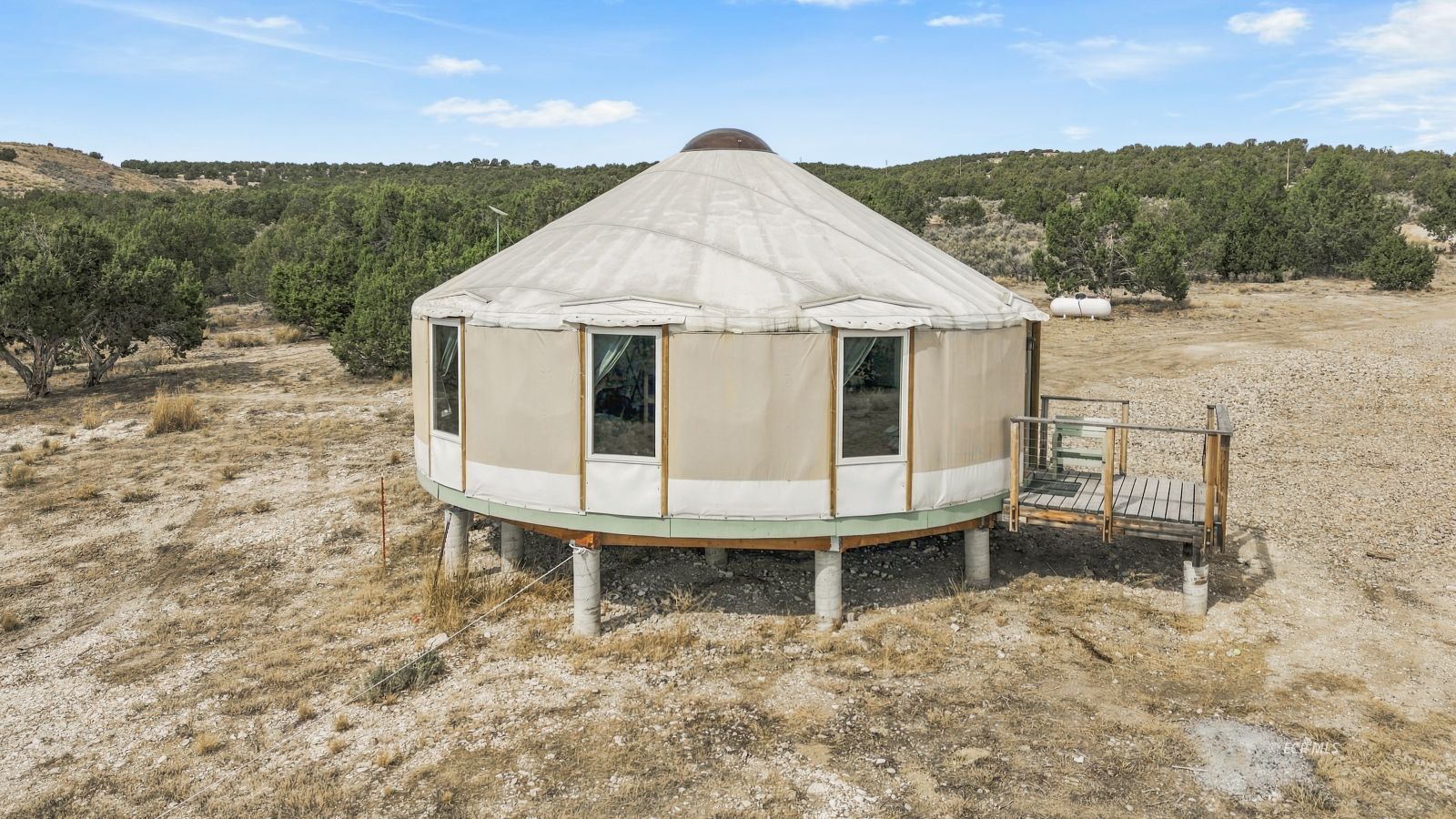 Round canvas yurt raised on concrete supports, with a small wooden deck in a dry, wooded landscape.