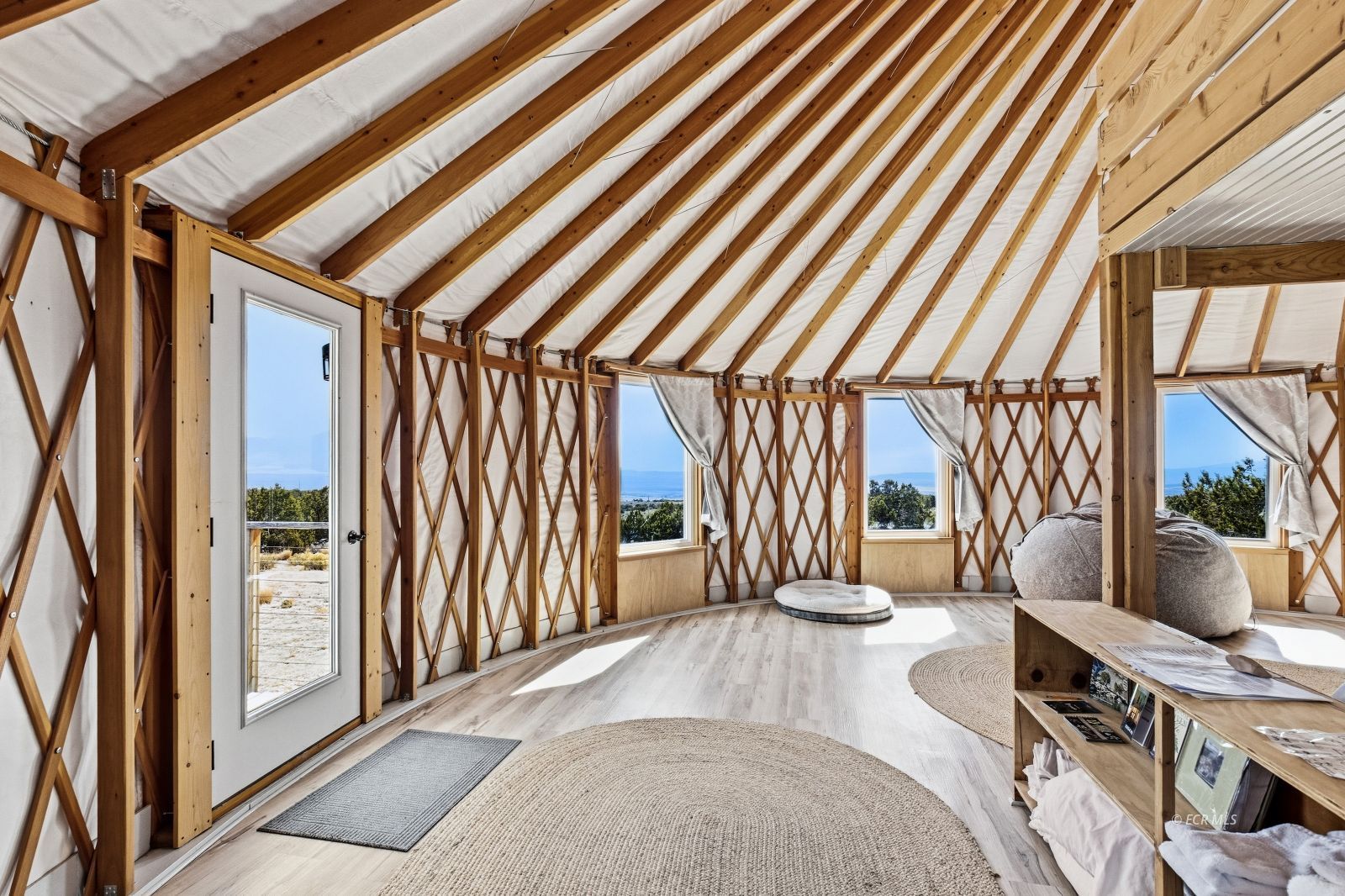 Living room with exposed timber framing, a fabric-covered vaulted ceiling, and windows overlooking the landscape.