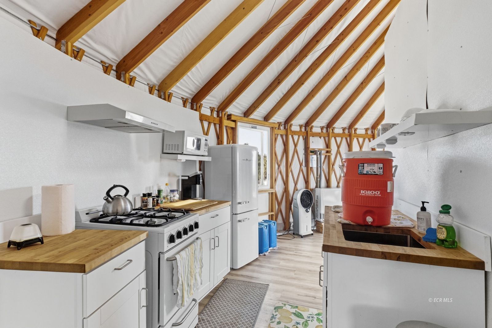 Compact kitchen with white cabinets, butcher-block counters, and exposed timber roof beams.