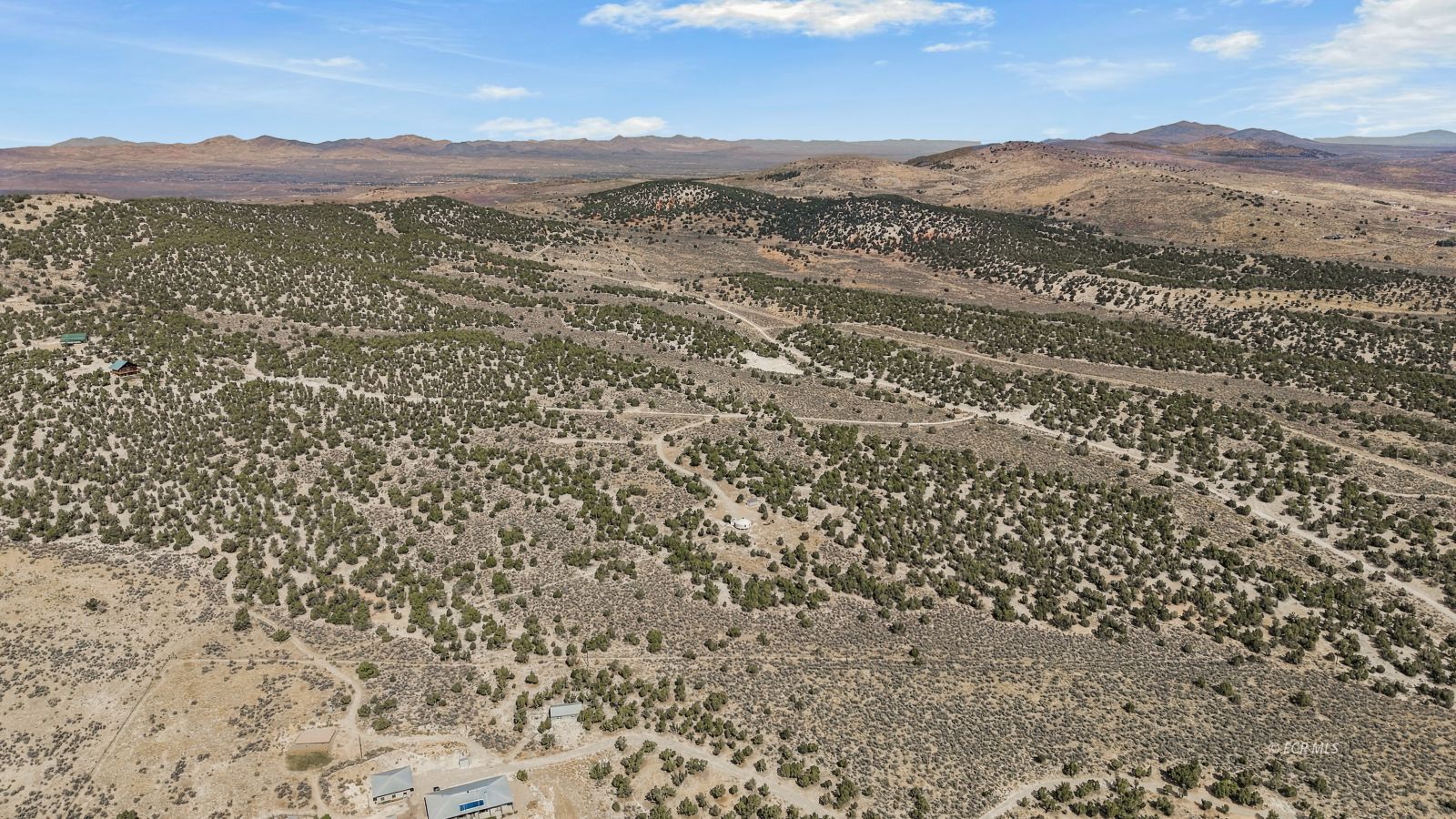Aerial view of a scrub-covered rural property with scattered buildings and distant hills.