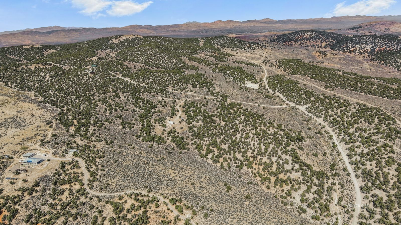 Aerial view of scrub-covered land with winding dirt roads and mountains in the distance.