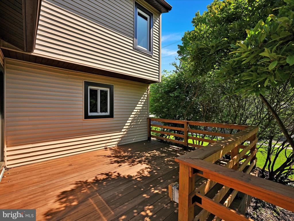 Wood deck beside a beige-sided house, bordered by wooden railings and leafy trees.
