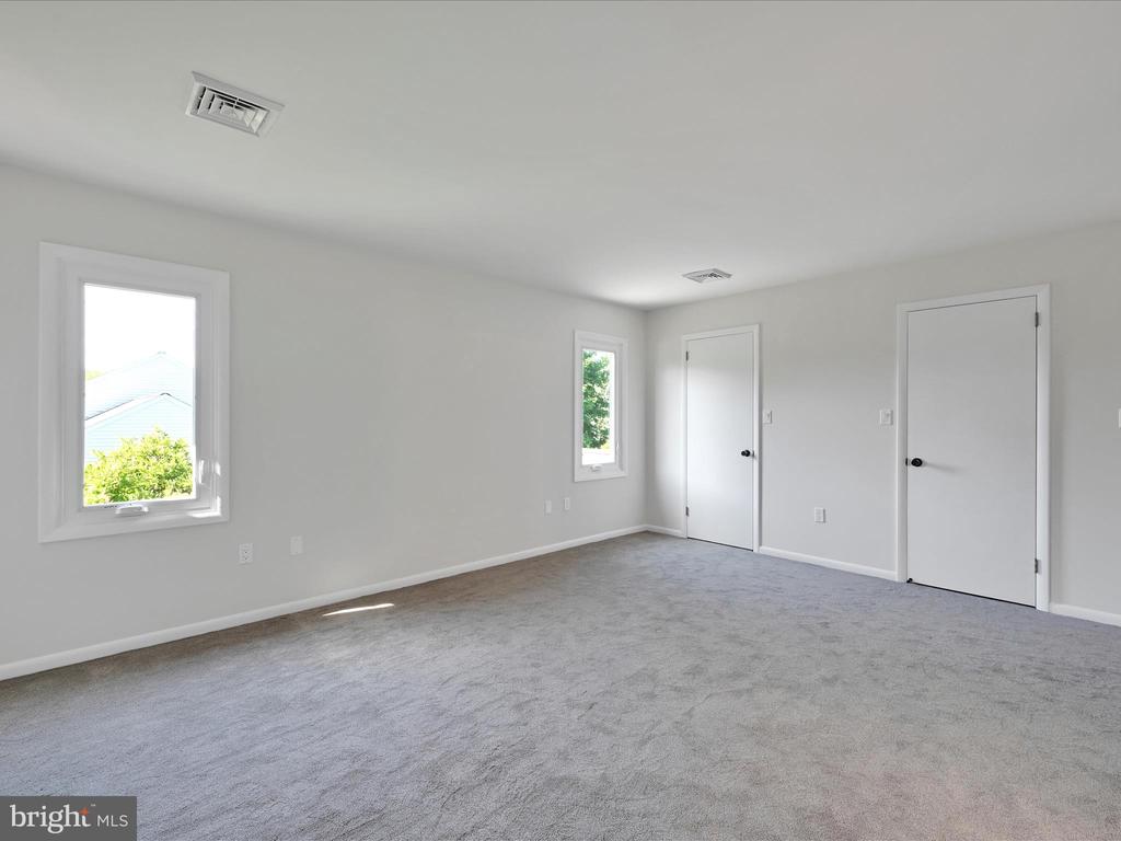 Empty carpeted room with light gray walls, two windows, and two white doors.