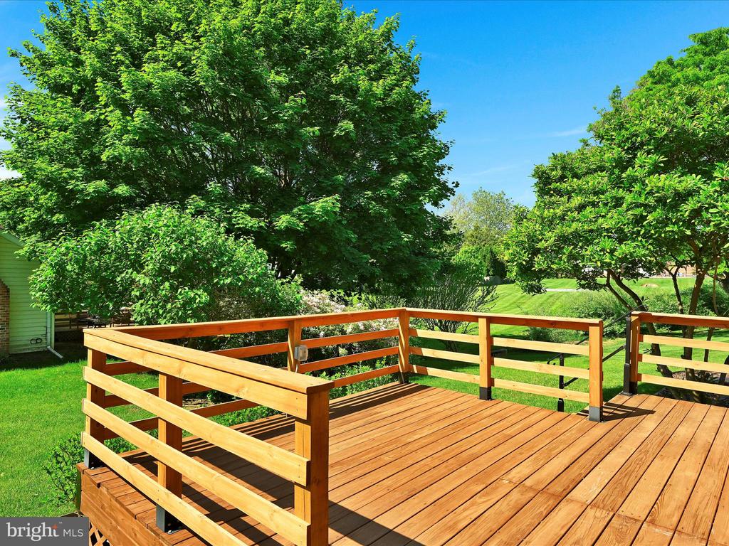 Wooden backyard deck with railings overlooking a green lawn and mature trees.