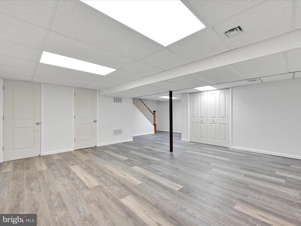 Finished basement with gray flooring, a support post, closet doors, and stairs.