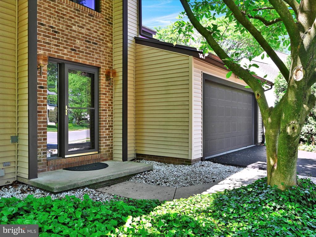 Home exterior with a brick entry, glass door, attached garage, and large shade tree.