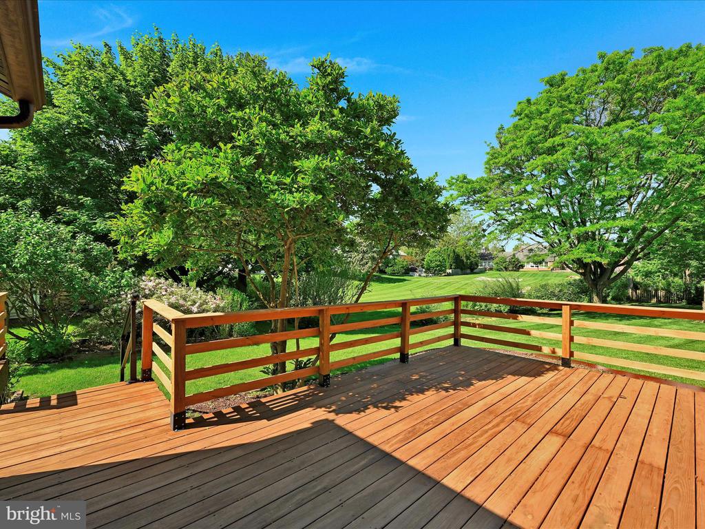 Wooden backyard deck overlooking a green lawn and mature trees.