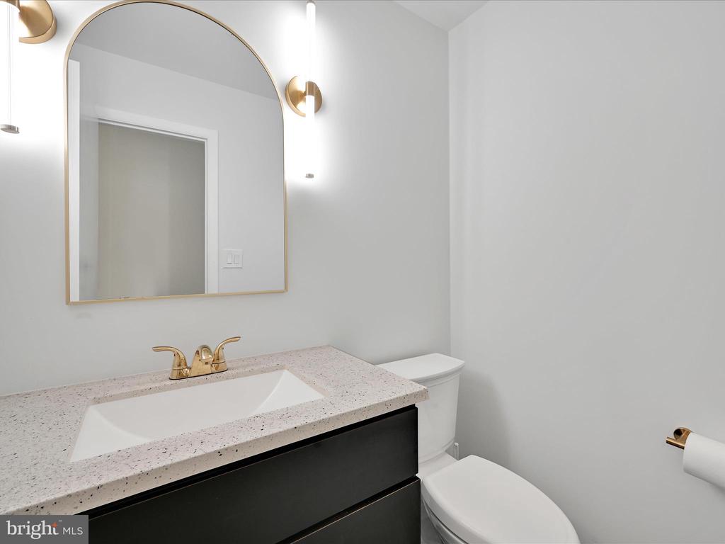 Bathroom with a speckled vanity countertop, dark cabinet, arched mirror, and gold-tone fixtures.
