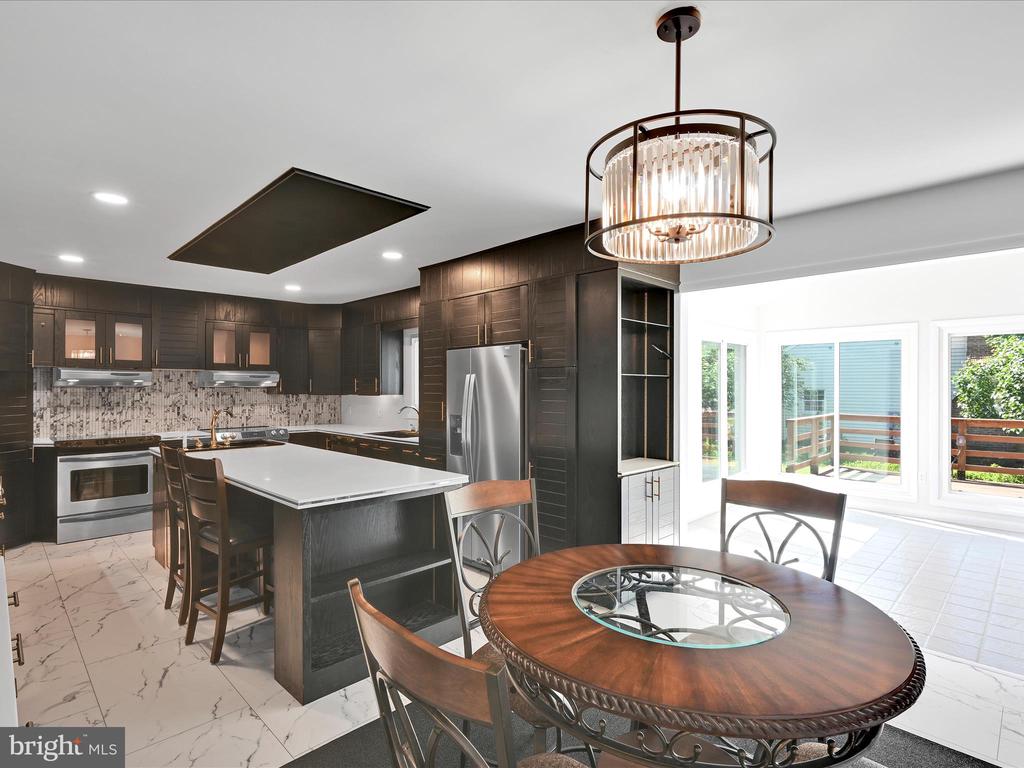 Kitchen with dark wood cabinets, a large white island, and a round dining table beside bright windows.