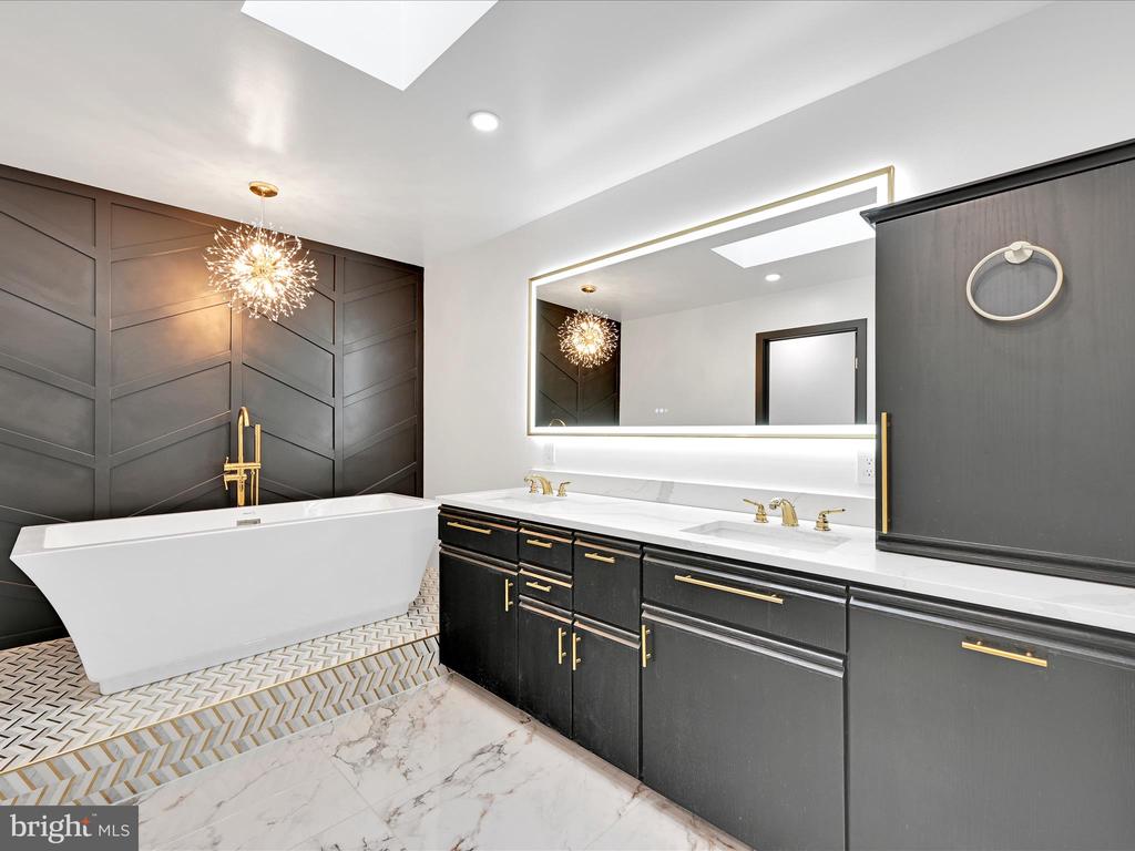 Modern bathroom with freestanding tub, dark paneled walls, and a double vanity with gold hardware.