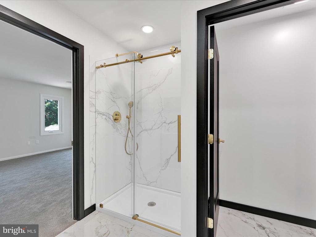 Bathroom with a glass-enclosed marble-look shower and gold-tone fixtures.