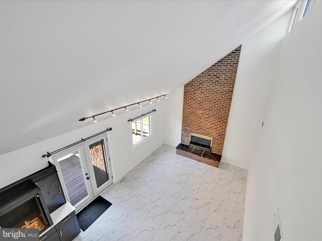 Vacant living room with tall brick fireplace, sloped ceiling, and glass doors to a deck.