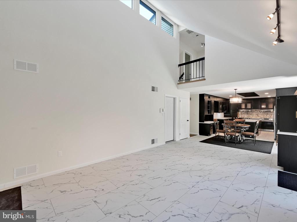 Open-plan living area with marble-look tile, a double-height ceiling, and a dark-cabinet kitchen beyond.