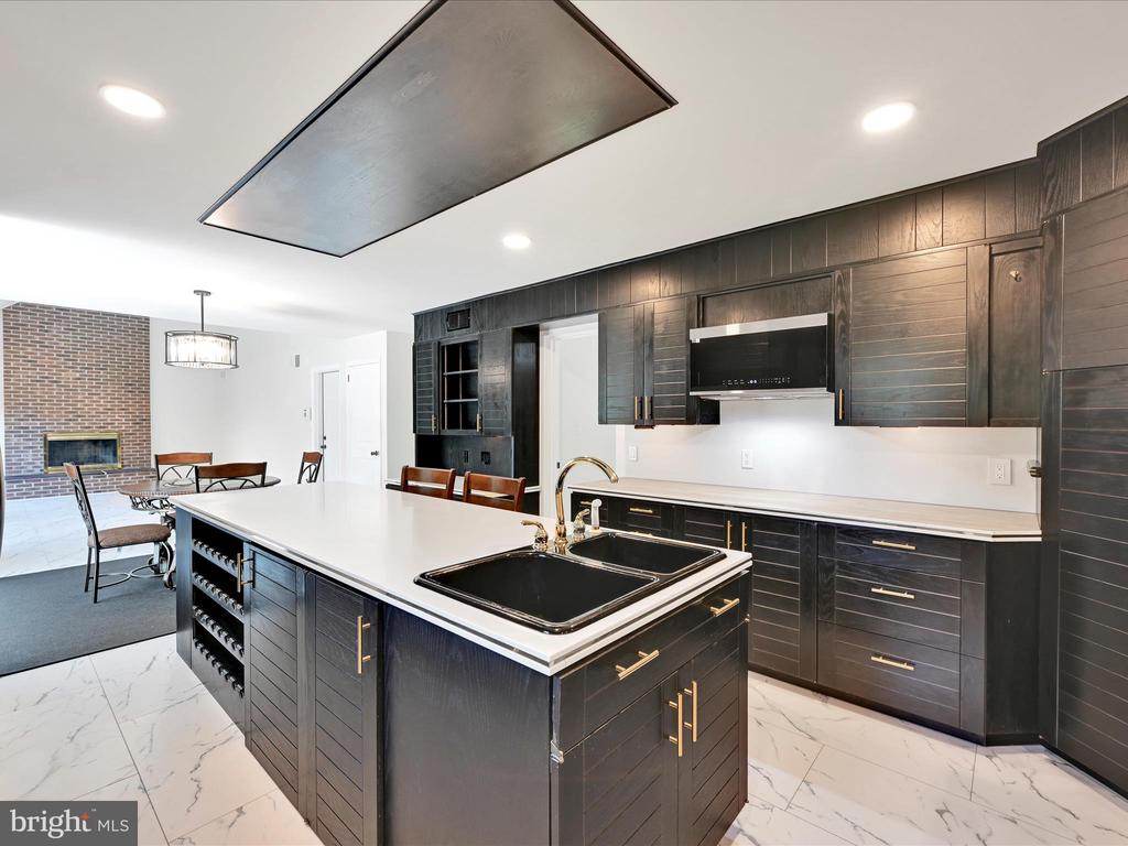 Kitchen with dark cabinetry, a large white island, black sink, and adjoining brick fireplace.