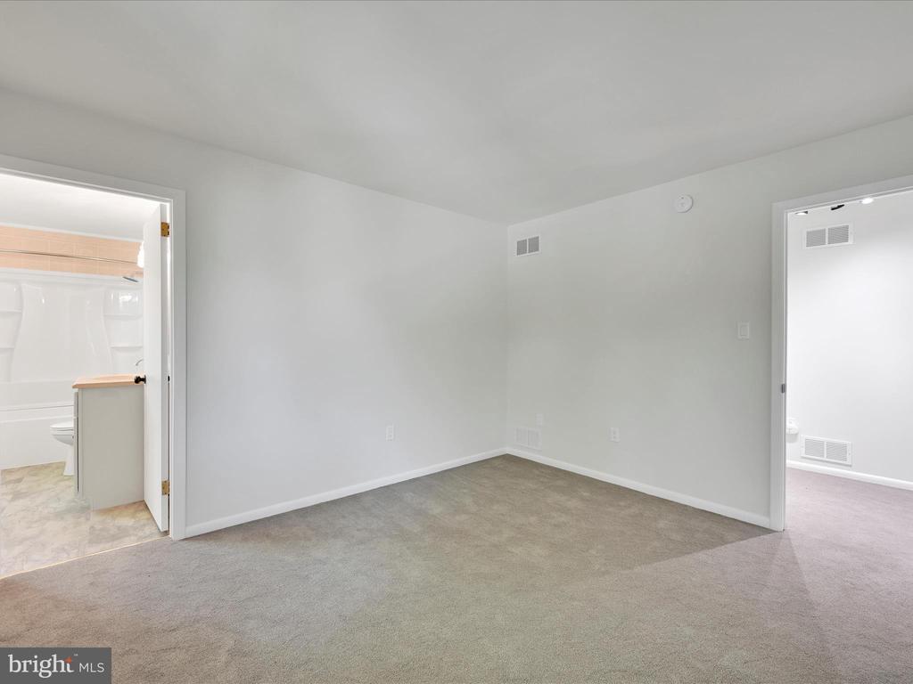 Empty carpeted bedroom with doorways to a bathroom and adjoining room.