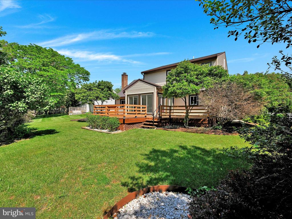 Home’s rear exterior with a raised wooden deck overlooking a broad, tree-lined lawn.