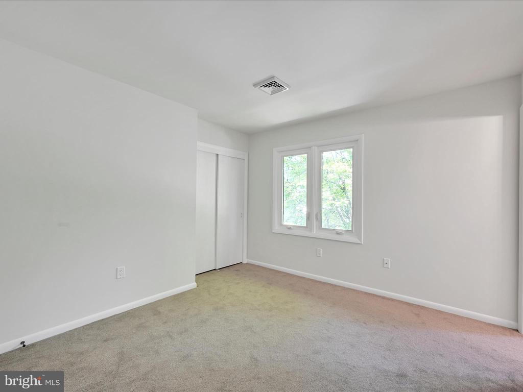 Empty bedroom with a sliding-door closet, carpeted floor, and double window overlooking trees.