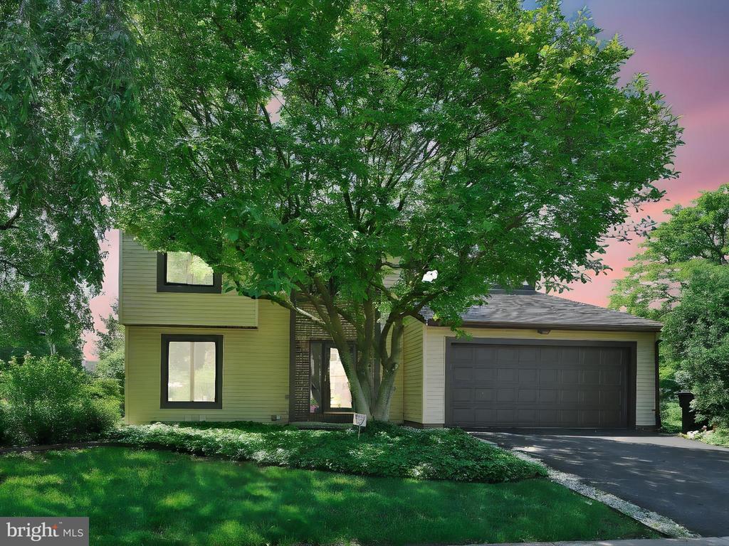 Two-story olive-sided house with a double garage, partly screened by a large leafy tree.