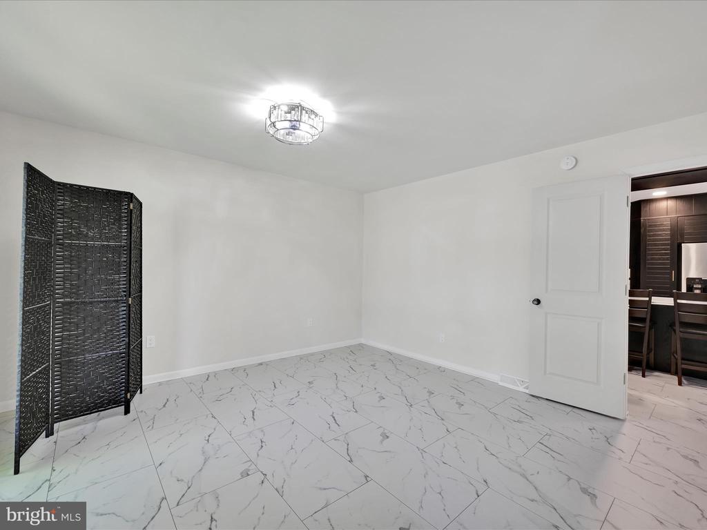 Empty tiled room with a black folding screen and an open doorway to the kitchen.