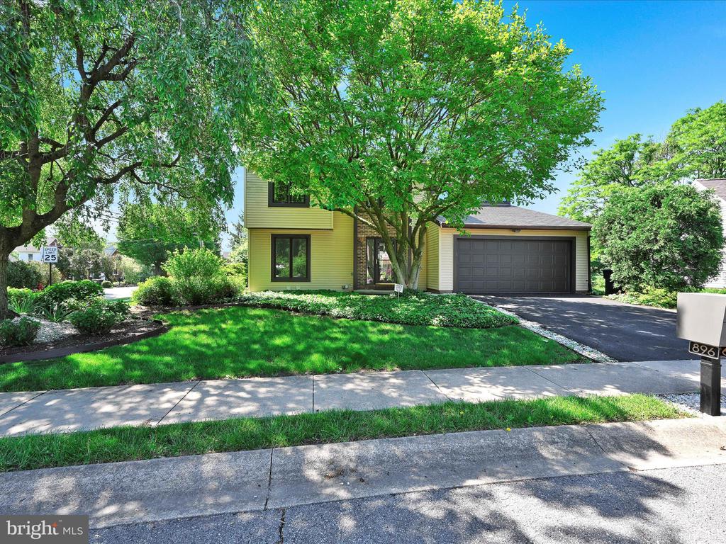 Yellow two-story home with a brick accent, attached garage, landscaped lawn, and mature shade trees.