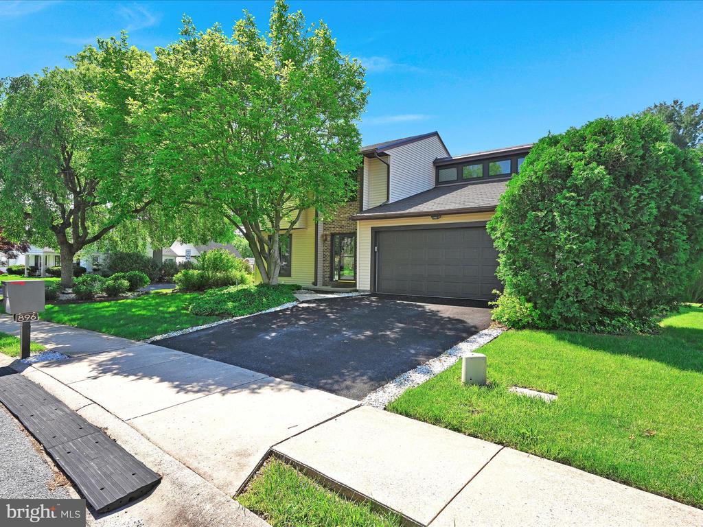 Two-story home with a dark garage door, paved driveway, and mature trees.